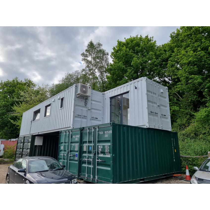 Custom container eco-home featuring white-finished upper level, green storage containers, climate control, and modern glazing by KC Cabins Solutions