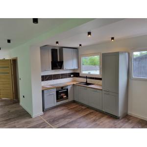 Modern container home kitchen featuring grey shaker-style units, wooden worktops, integrated appliances, and marble-effect splashback by KC Cabins Solutions