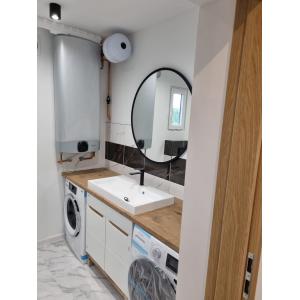 Modern container home utility room featuring integrated laundry, hot water system, wooden worktop, and designer black round mirror with marble-effect tiling