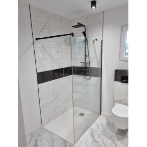 Luxury walk-in shower in converted shipping container featuring marble-effect white tiles, black accent strip, frameless glass screen, rainfall showerhead, and modern black fixtures - KC Cabins premium bathroom conversion