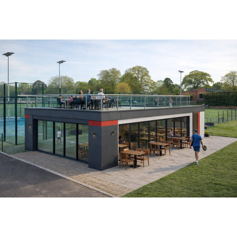 Modular padel club café building in the UK with rooftop terrace overlooking outdoor padel courts, featuring aluminium glazing, flat roof and contemporary cladding.
