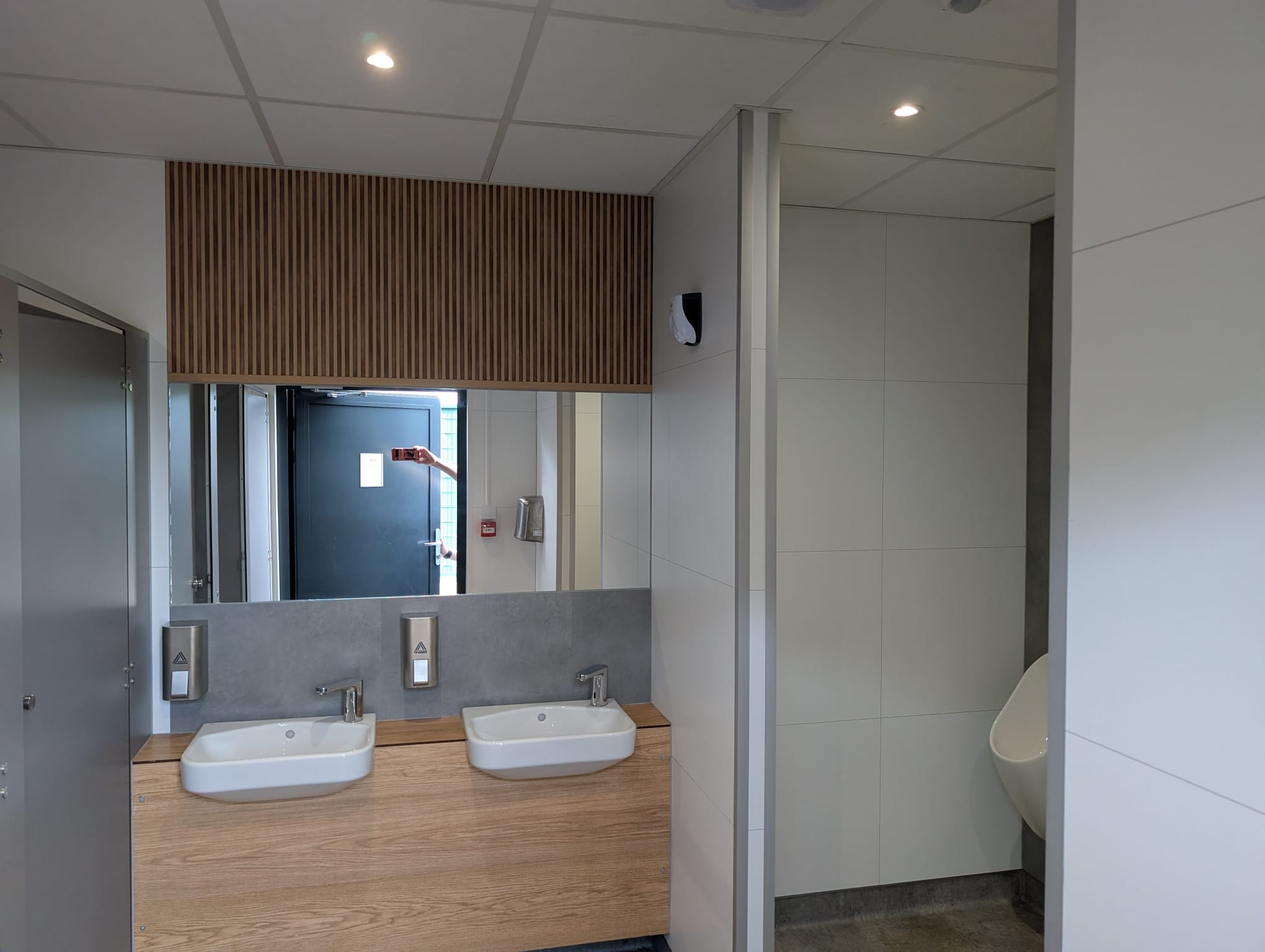 Washroom area with twin basins, large mirror, soap dispensers and timber-effect vanity finish.