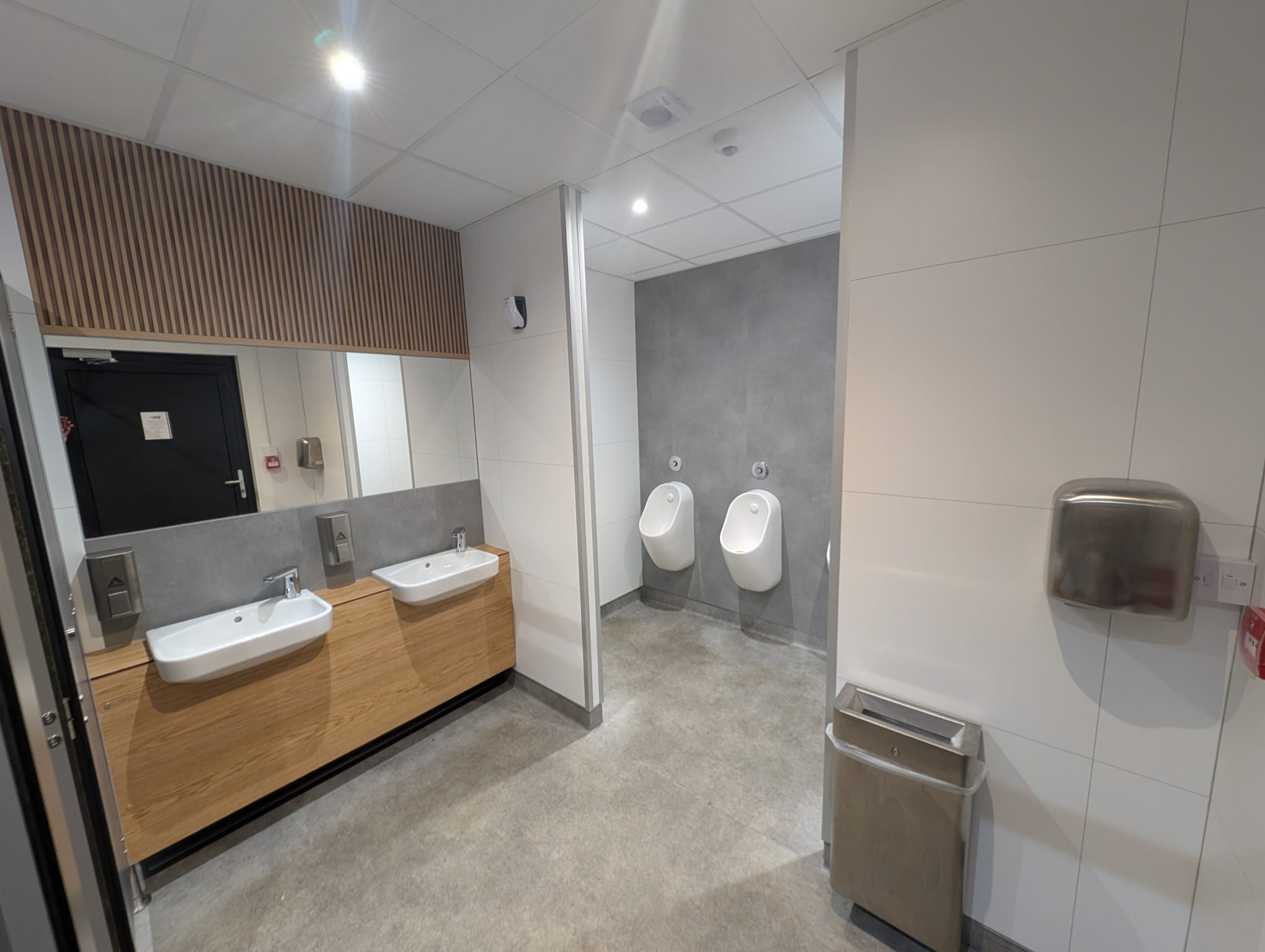 Double washbasin area inside the modular welfare unit with mirror, dispensers and slatted timber-effect feature panel.