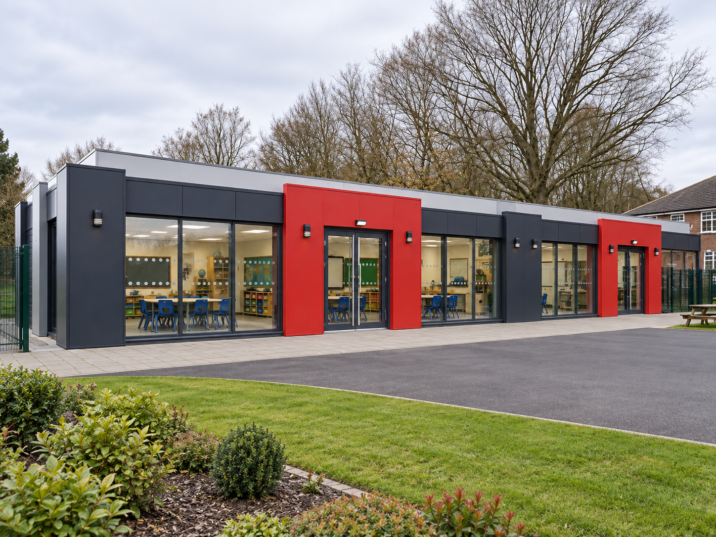 Long classroom-setting building with two red entrance surrounds and dark-grey cladding.
